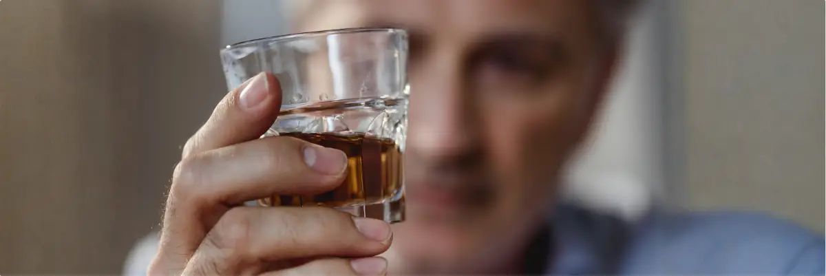 Close-up of a person holding a glass of liquor, with a blurred face in the background.