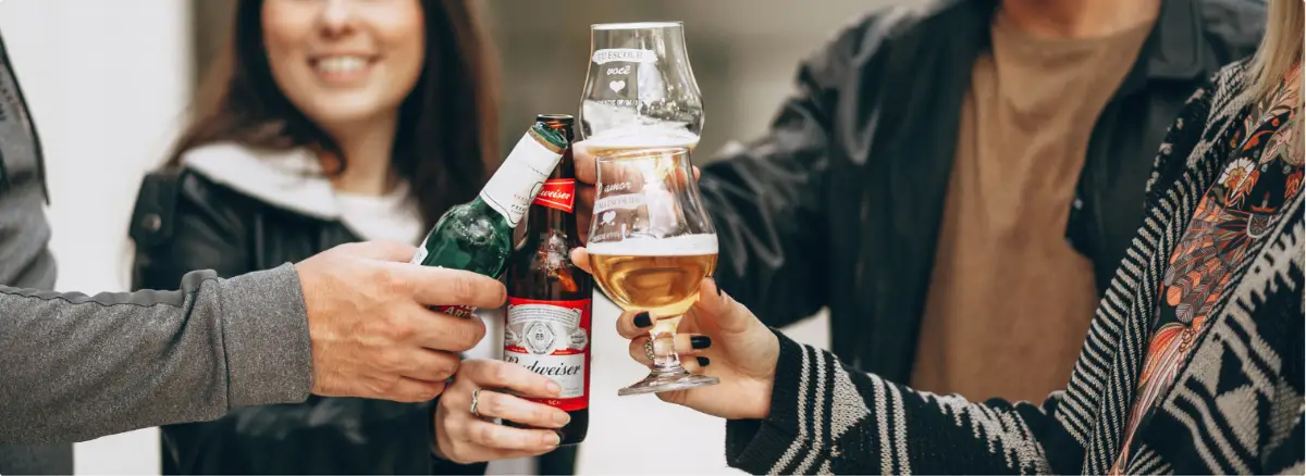 Group of adults clinking beer bottles and a wine glass in a social setting.