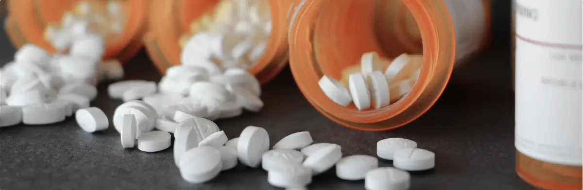 Prescription pill bottles spilled open with white opioid tablets on a surface.