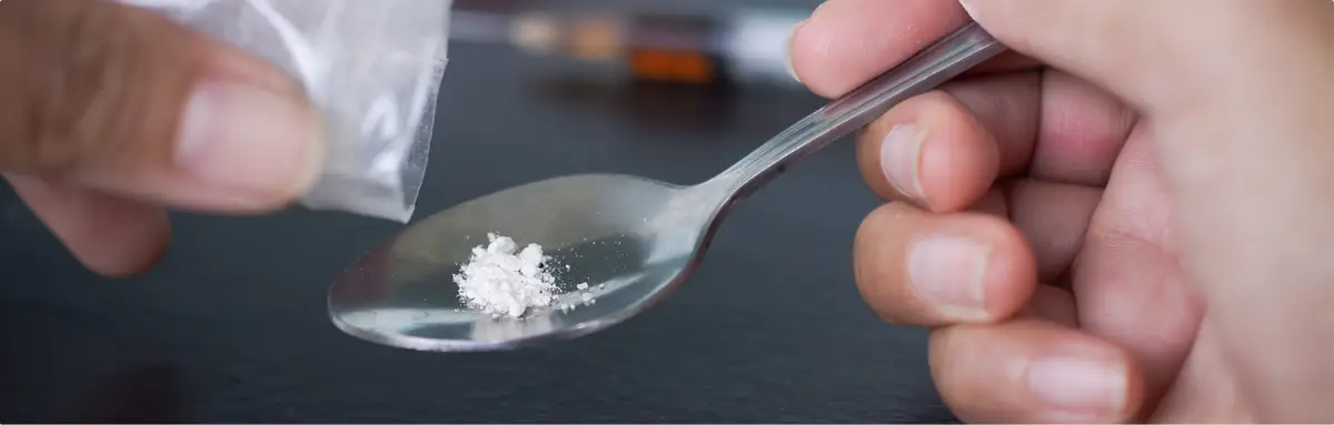 Close-up of hands holding a spoon with white powder, representing opioid misuse.