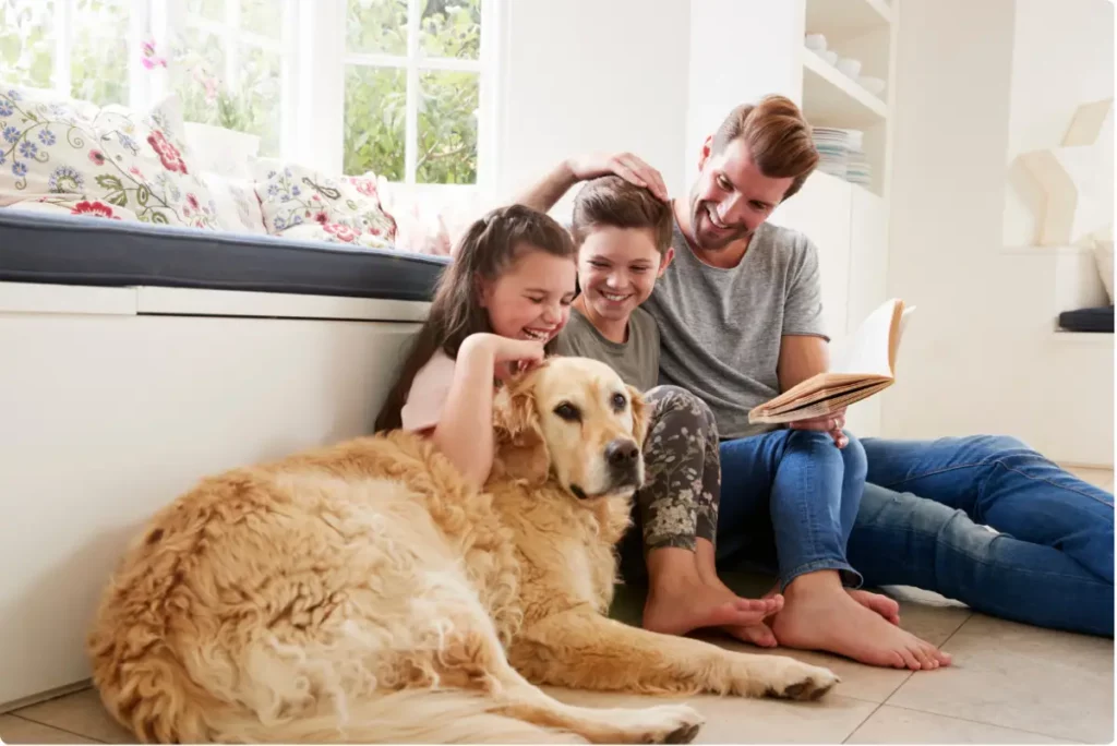 Family sitting together at home with a dog, smiling and reading, representing stability and support through an aftercare program.